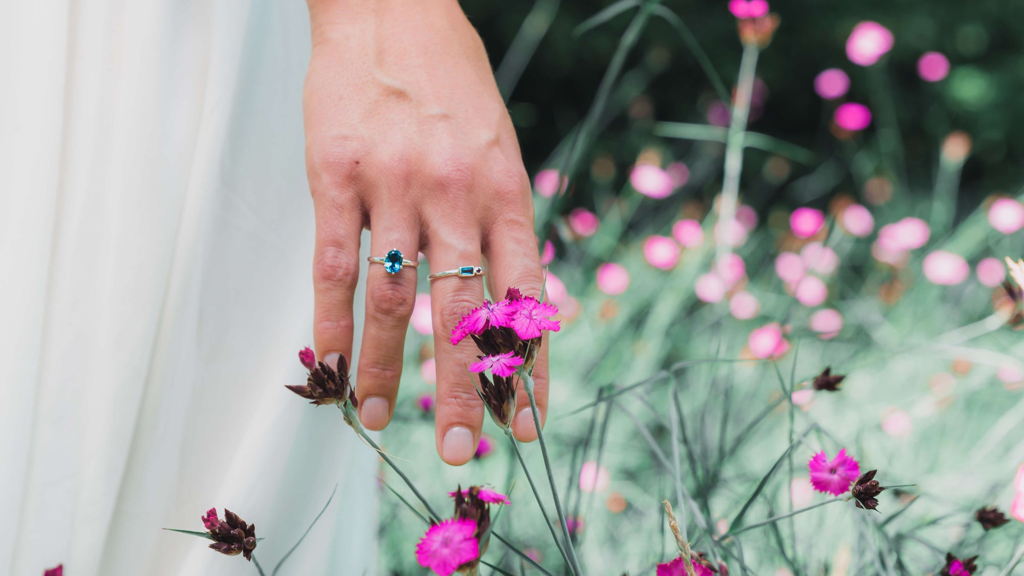 Frauenhand zwei Ringe Sterling Silber blauer Topas weißes Brautkleid pink blühende Blumen